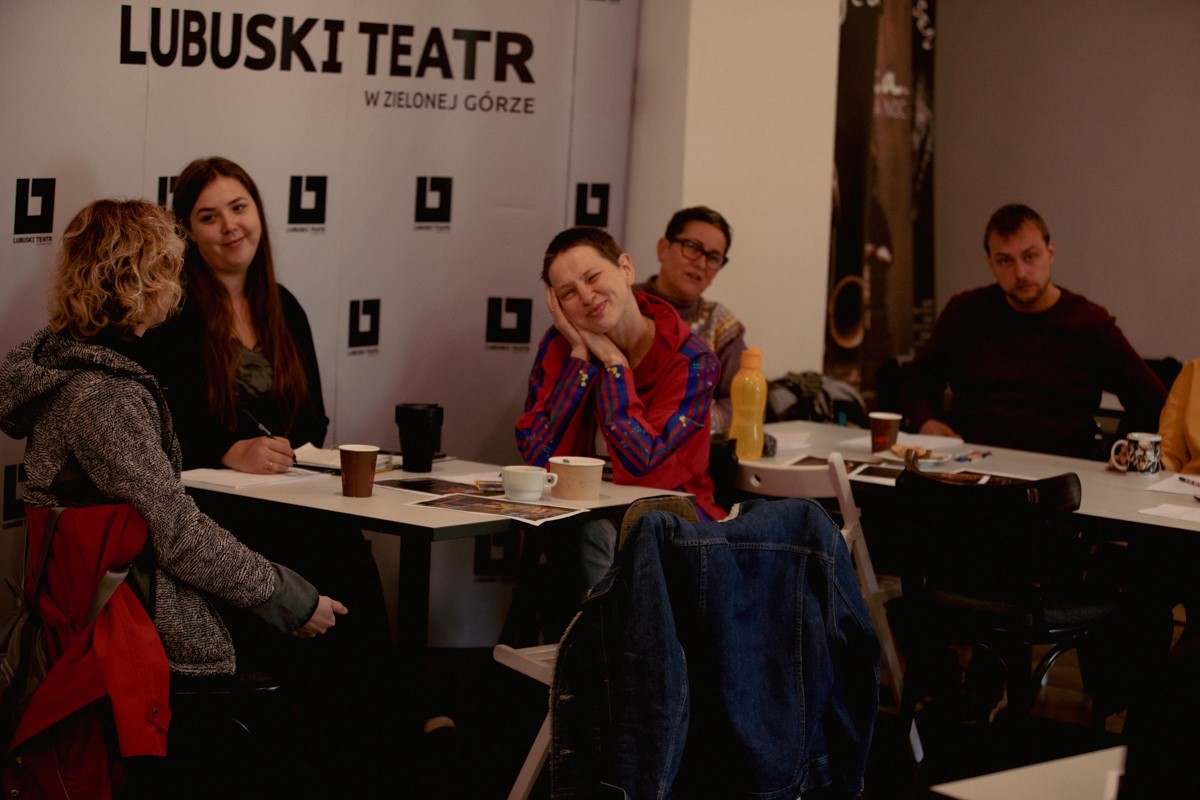 Pięcioro pracowników teatru - administracyjni i aktorzy, uczestniczą z uśmiechem w szkoleniu na temat audiodeskrypcji. 